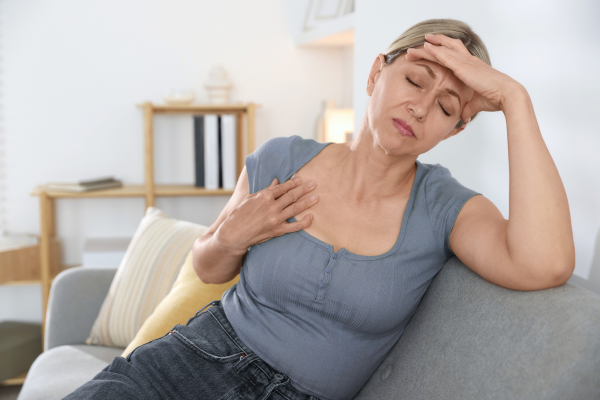 why perimenopause can feel like anxiety; middle aged woman feeling warm and holding her head, sitting on a couch
